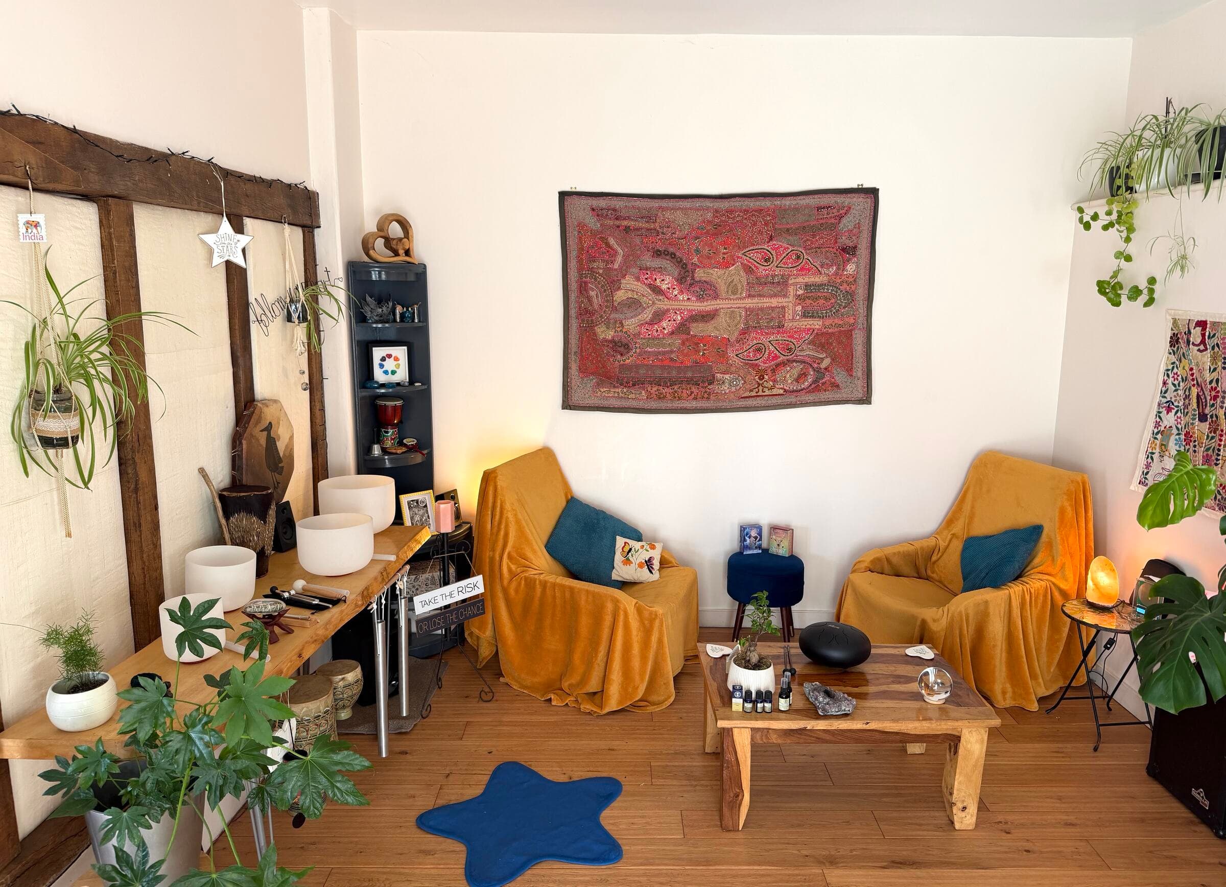 The therapy room at The Sawyers: two ochre armchairs either side of a low wooden table, crystal singing bowls on a live-edge bench, plants and an exposed timber frame
